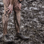 hands pressed onto knees, mud covered legs on a background of mud