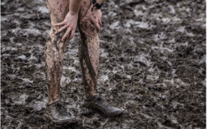 hands pressed onto knees, mud covered legs on a background of mud